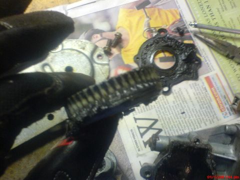 1986 Ford Bronco - A close-up view of a greasy engine part, possibly a gear, with visible teeth, laid out on a newspaper.