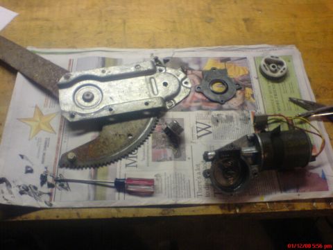 1986 Ford Bronco - Window regulator and motor parts laid out on a table for repair or inspection.