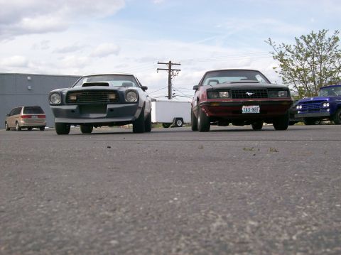 1978 Ford Mustang II - Two cars and a van are parked on an asphalt lot under a cloudy sky.
