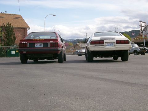 1978 Ford Mustang II - Two cars are parked in a lot, viewed from the rear.