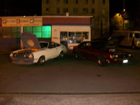 1978 Ford Mustang II - Two coupes, one white and one red, are parked outside a building at night with their hoods open.