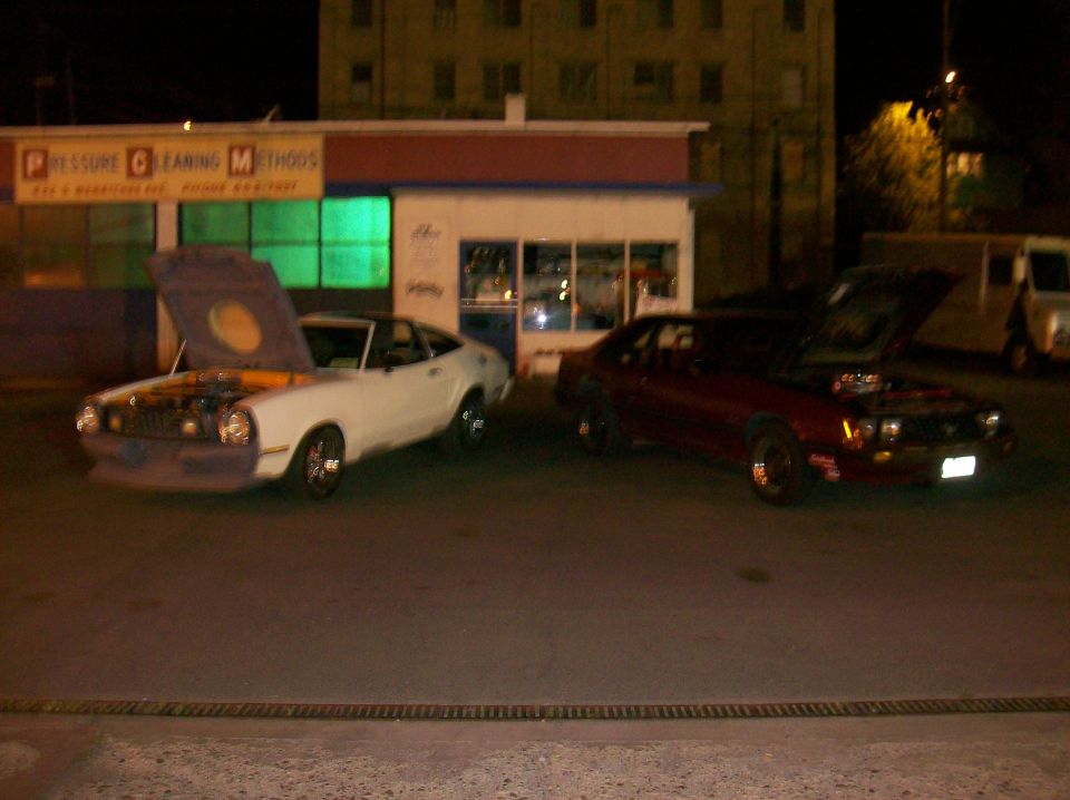 White 1975 Ford Mustang II coupe with hood open, parked next to a red coupe