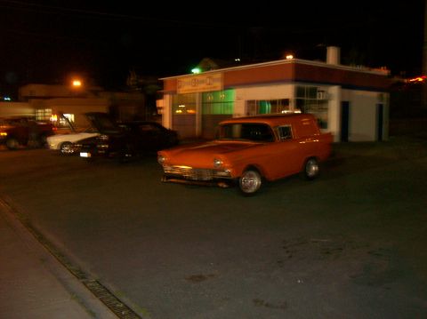 1978 Ford Mustang II - An orange 1956 Ford sedan delivery is parked outside a building at night, with other vehicles visible.