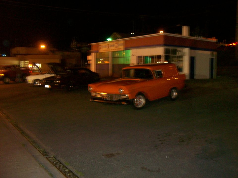 Orange 1956 Ford sedan delivery with chrome grille and custom wheels, parked at night