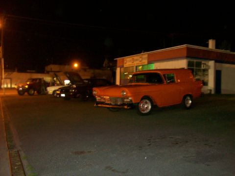 1978 Ford Mustang II - An orange 1956 Ford panel van is parked in front of a building at night, with other vehicles visible in the background.