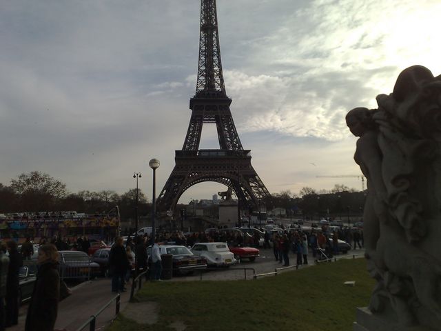 Eiffel Tower with many cars parked in front, people milling around