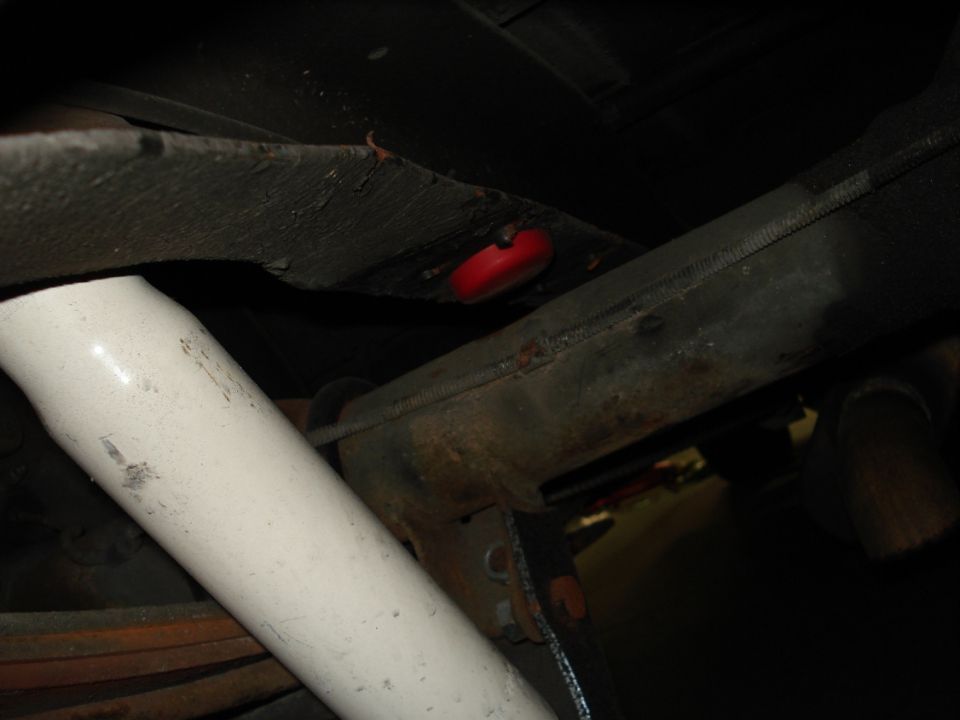 Underside of a vehicle showing suspension components and a red rubber part. Text at bottom reads SUPERMOTORS