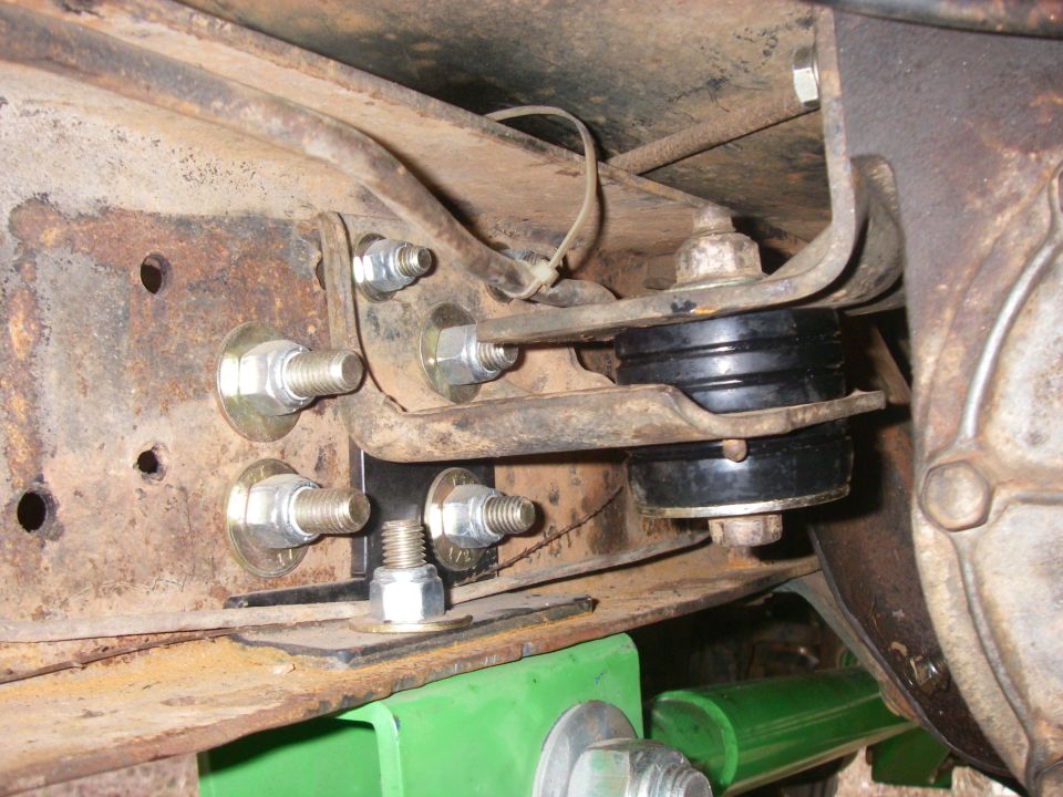 Close-up of rusty vehicle frame with new black rubber body mounts and silver bolts
