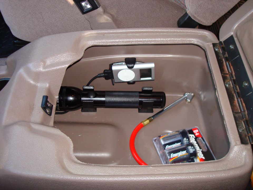 Center console storage compartment with flashlight, camera, tire gauge, and batteries