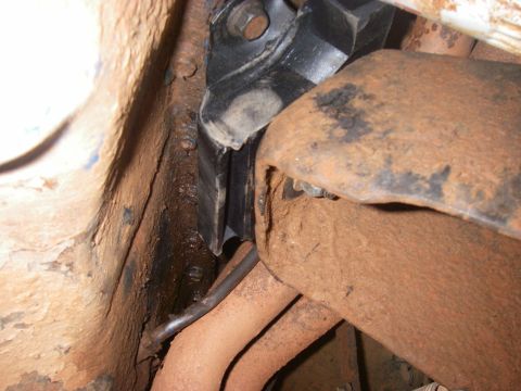 1978 Ford Bronco - Close-up view of rusted vehicle frame components, including exhaust pipes and an engine mount.