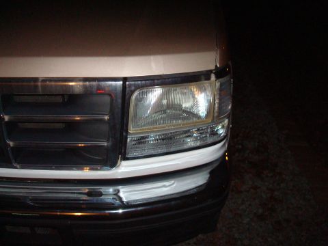 1992 Ford Bronco - The front grille and headlight assembly of a light-colored Ford truck are visible at night.