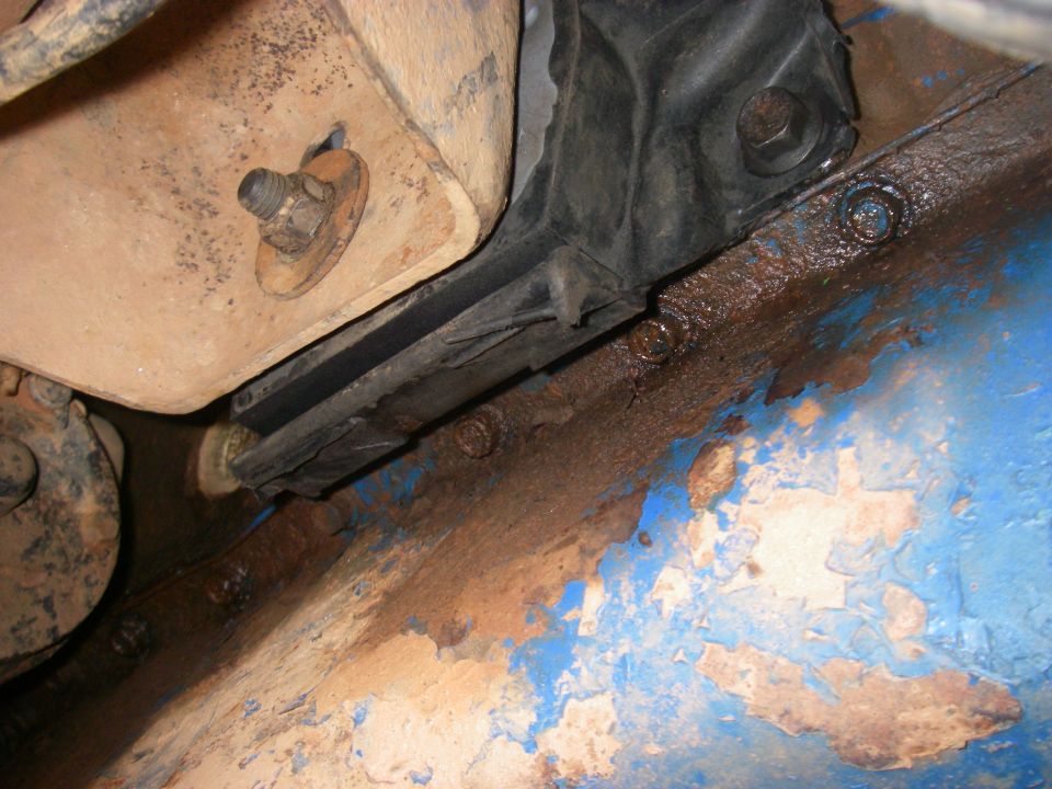 Rusty engine mount and oil pan against a flaking blue frame rail underneath a truck