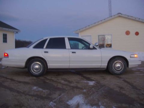 1996 Ford Crown Victoria - Side view of a white 1996 Ford Crown Victoria sedan parked on a dirt lot.