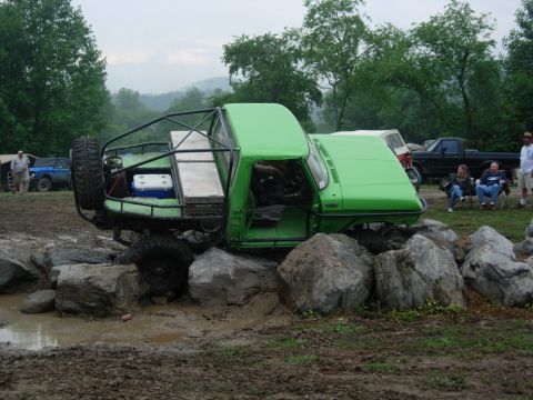 1978 Ford Bronco - A modified green off-road vehicle navigates a rocky obstacle course, with other vehicles and spectators in the background.