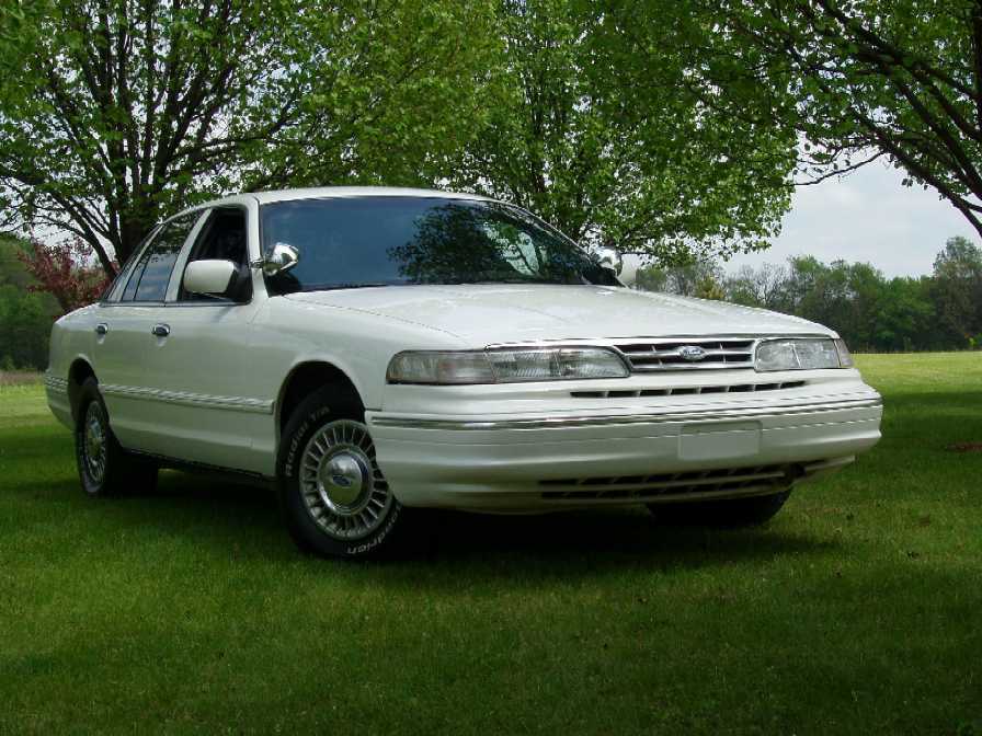 White Ford Crown Victoria sedan, front 3/4 view, parked on green grass with trees behind