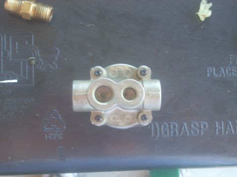1992 Ford Bronco - A metal valve part is shown on a black surface with some text and a brass fitting.