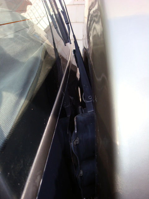 2000 Mitsubishi Montero - A close-up view of a windshield wiper assembly on a dark vehicle, positioned next to a light-colored body panel.