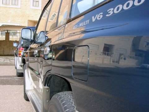 2000 Mitsubishi Montero - A dark SUV is seen from the side, a 'V6 3000' badge and a fuel door. Another vehicle is visible in the background.