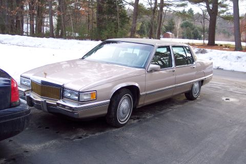 2001 Ford Crown Victoria - This tan Cadillac sedan is parked next to another vehicle with snow on the ground.