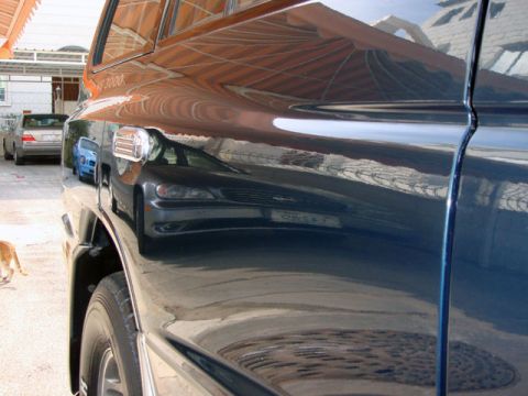 2000 Mitsubishi Montero - Reflections on the side of a dark SUV obscure details of the vehicle and its surroundings.
