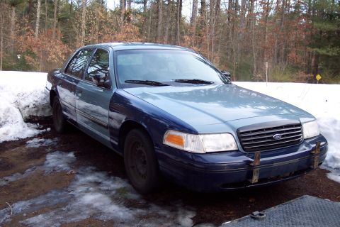 2001 Ford Crown Victoria - A two-tone blue sedan sits in a snowy, wooded area.