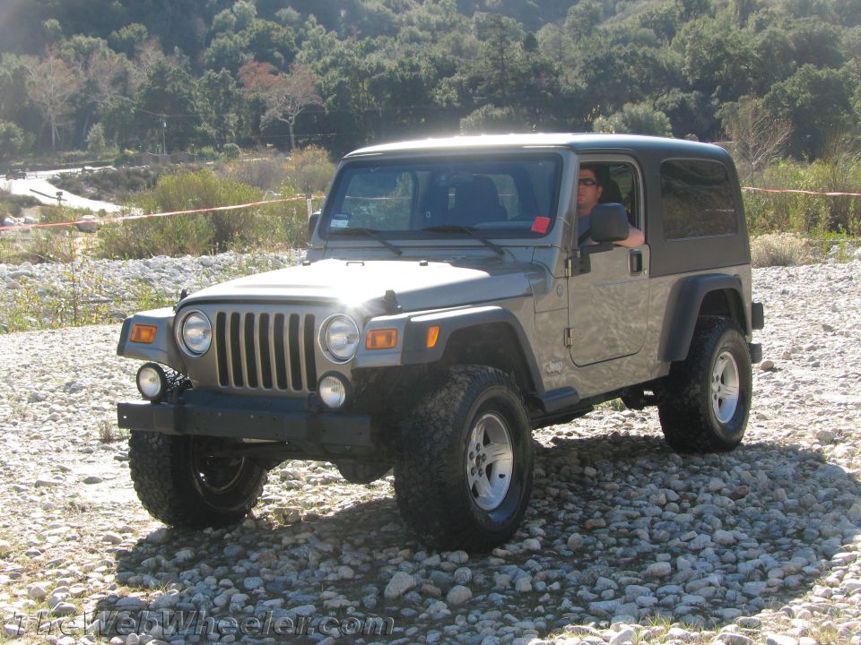Gray Jeep Wrangler parked on a rocky surface with trees in the background