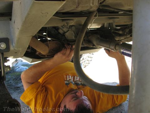 1987 Suzuki Samurai - A person works on the underside of a vehicle, focusing on the drivetrain and exhaust components.