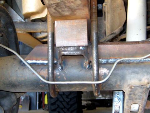 1996 Ford Bronco - Close-up of a metal block installed between a leaf spring and the vehicle's frame.