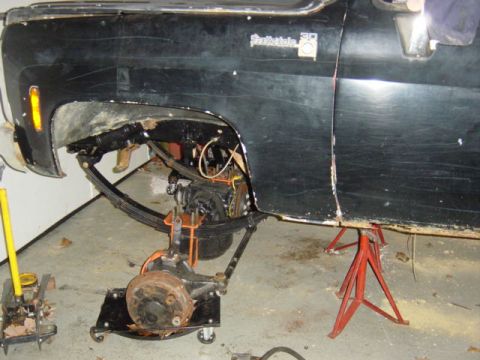 1987 Suzuki Samurai - Side view of a black truck with its front wheel assembly removed and supported by a dolly and jack stands.