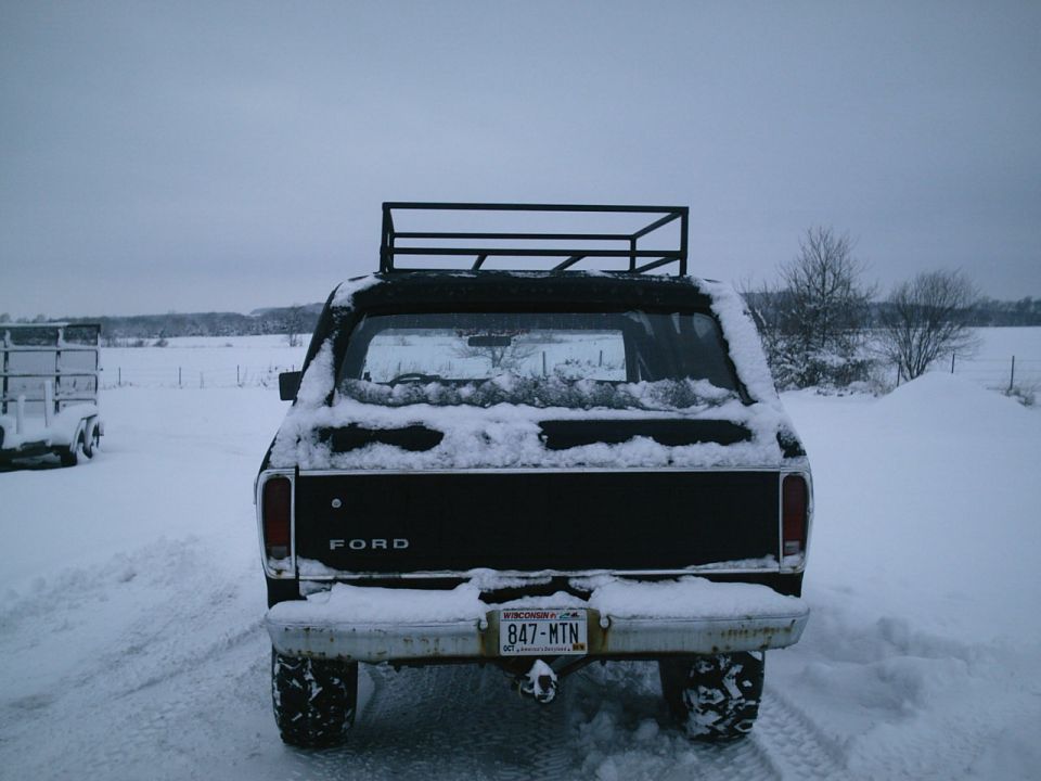 Rear view of a black 1979 Ford Bronco in the snow with a roof rack