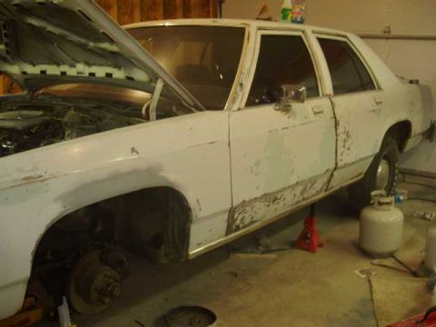 1996 Ford Crown Victoria - A white sedan, possibly from the early 1980s, is undergoing repairs with its hood up and body in primer.