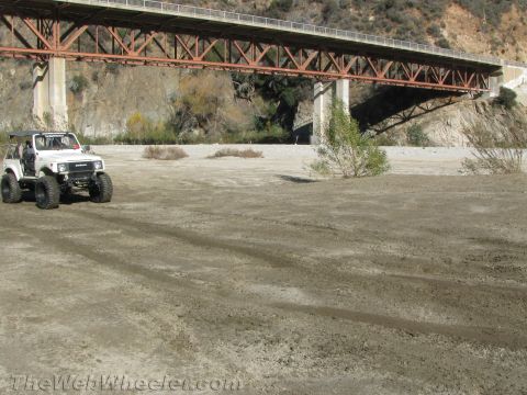1987 Suzuki Samurai - A white 1987 Suzuki Samurai navigates a dry riverbed beneath a large bridge.