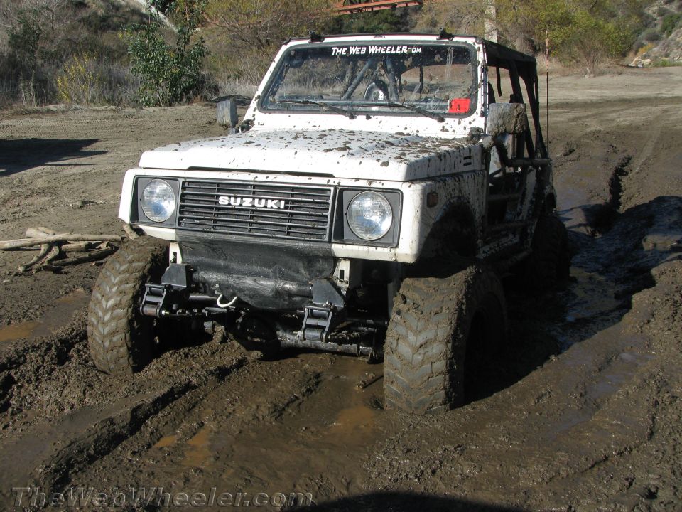 White Suzuki Samurai stuck in mud, front view. It has a roll cage and off-road tires