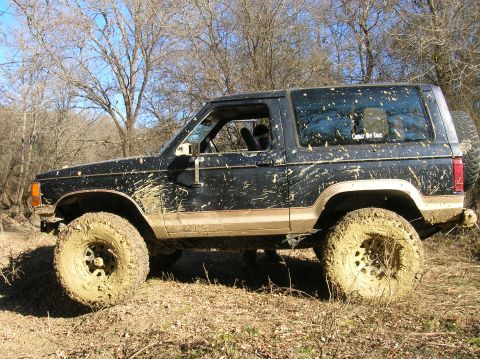 1996 Ford Bronco - This SUV is heavily coated in mud, suggesting it has been driven off-road. The tires are large and suitable for rough terrain.