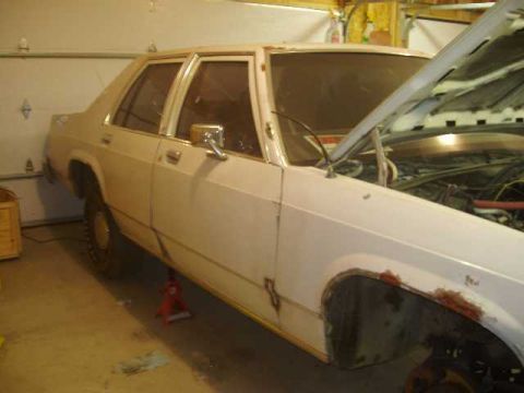 1996 Ford Crown Victoria - This white sedan, possibly a Ford, is shown with its hood open and visible rust around the front wheel well.