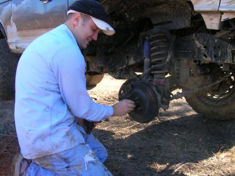 1996 Ford Bronco - A man is kneeling down and appears to be working on the brake assembly of a vehicle.