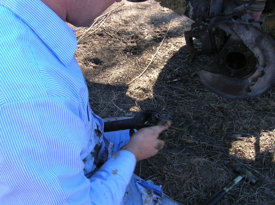 Person in blue striped shirt working on a vehicle's suspension component on the ground