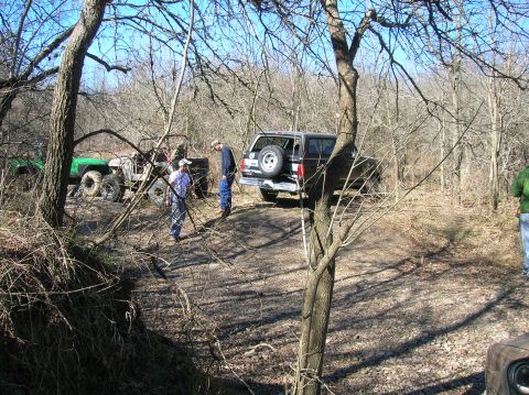 1996 Ford Bronco - People gather around off-road vehicles in a wooded area on a sunny day.