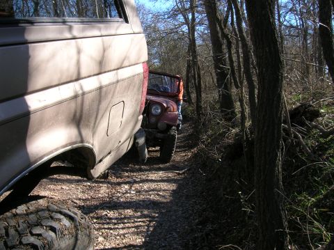1996 Ford Bronco - Two off-road vehicles, a tan Ford Bronco and a red Jeep, navigate a wooded trail.