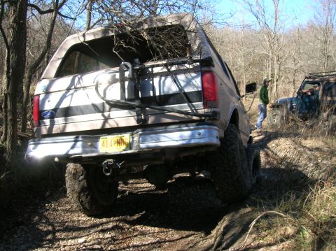 1996 Ford Bronco - A lifted 1996 Ford Bronco is seen from the rear, parked on a dirt trail with another off-road vehicle in the background.