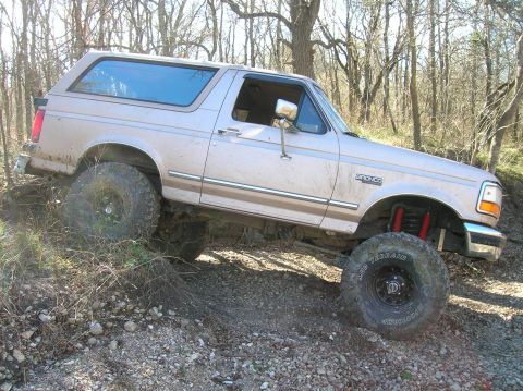 1996 Ford Bronco - A tan Ford Bronco navigates a dirt path with large off-road tires.