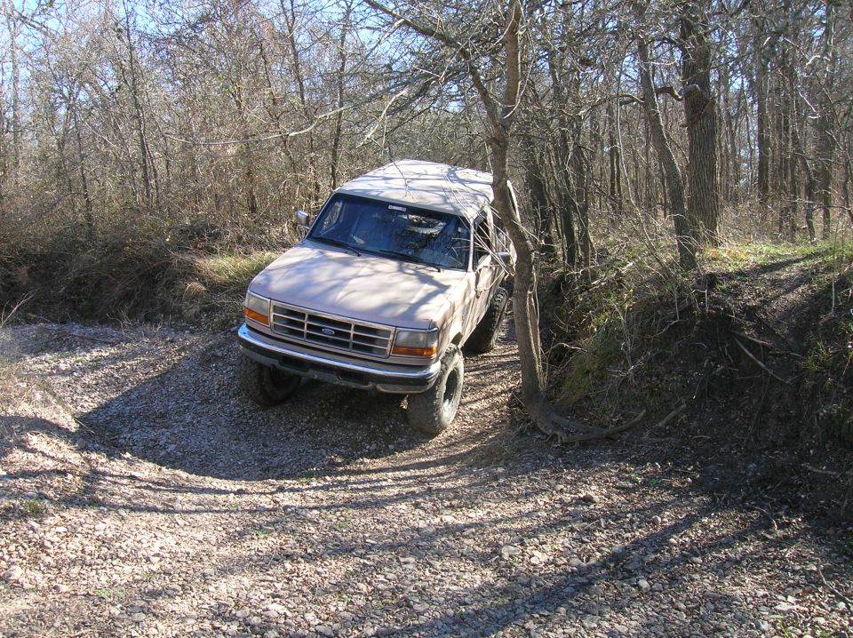 Tan 1996 Ford Bronco driving on a gravel path through trees