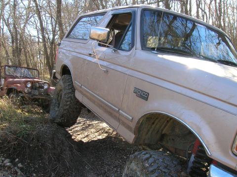 1996 Ford Bronco - Two off-road vehicles, a 1996 Ford Bronco and a red Jeep CJ, navigate a challenging dirt path.