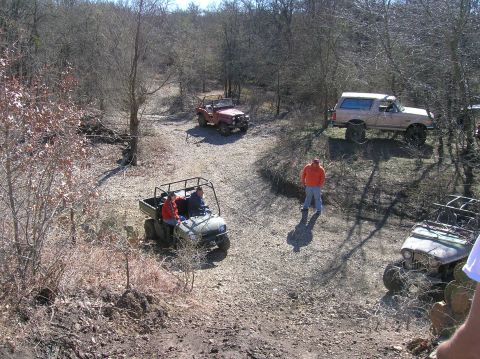 1996 Ford Bronco - Several off-road vehicles are gathered on a dirt trail surrounded by trees.