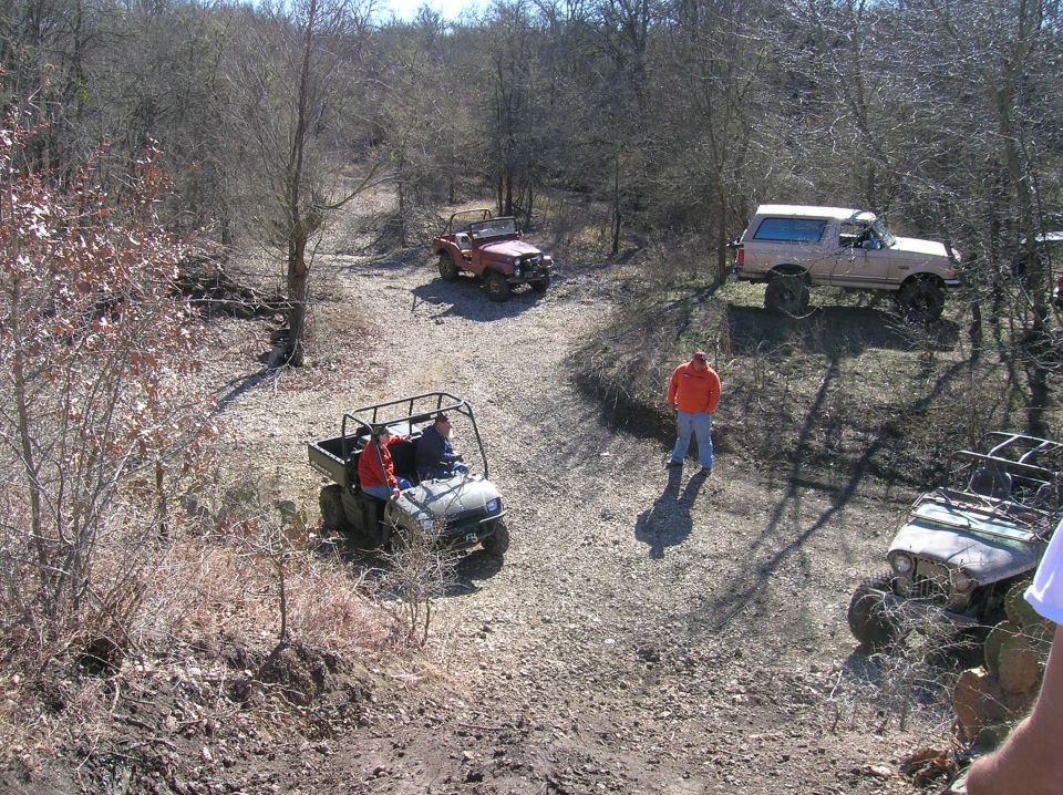Tan Ford Bronco with a white roof, seen from a 3/4 front angle on a dirt path