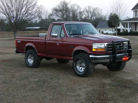 1992 Ford F-150 - Dark red Ford F-150 regular-cab long-bed 4x4 parked on winter grass, shown from the passenger-side front three-quarter angle. It has a blac…