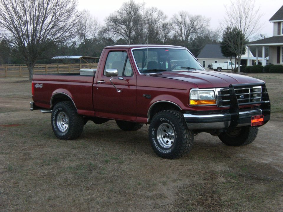 Dark red Ford F-150 regular-cab 4x4 in a field, front three-quarter view with brush guard