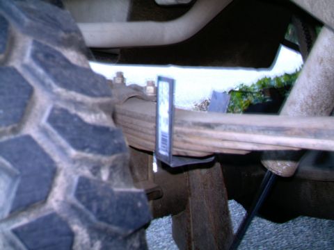 1987 Ford Bronco II - A measurement tool is attached to the leaf spring of a vehicle, near the tire.