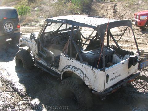 1987 Suzuki Samurai - Muddy 1987 Suzuki Samurai off-roading with other vehicles nearby.
