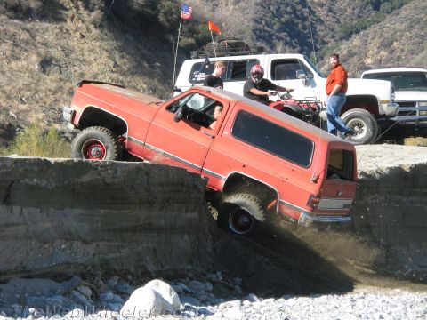 1987 Suzuki Samurai - Off-roading action with a red SUV tackling a challenging dirt obstacle.